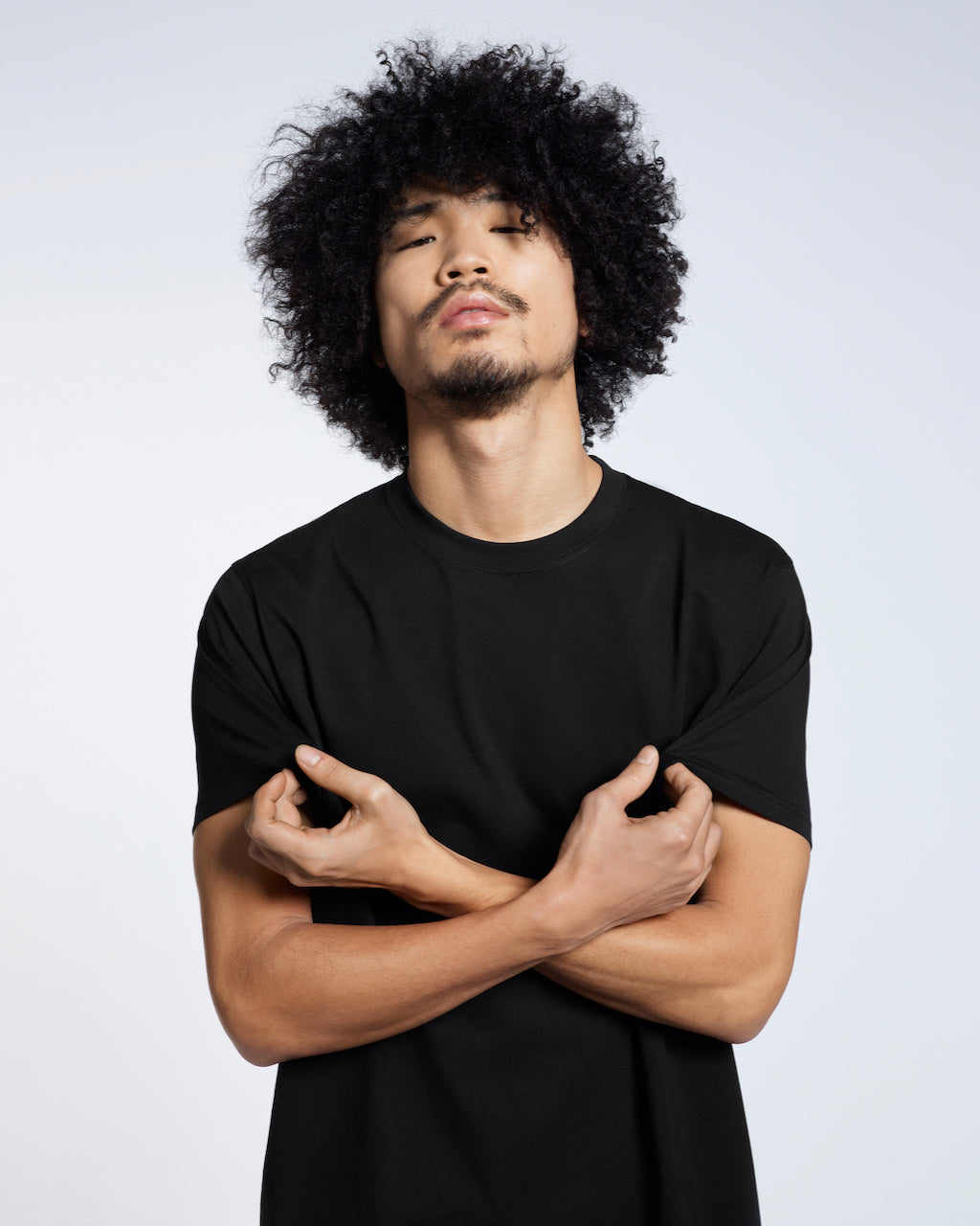 A man looking into the camera, touching his plain black short sleeve organic cotton t shirt.