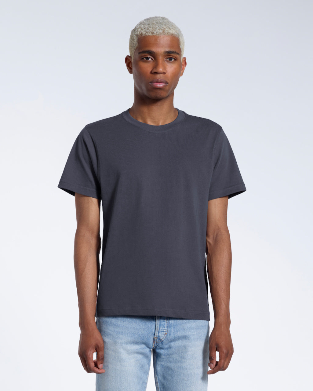 A man facing front on looking into the camera, modelling a plain dark grey short sleeve organic cotton t shirt.