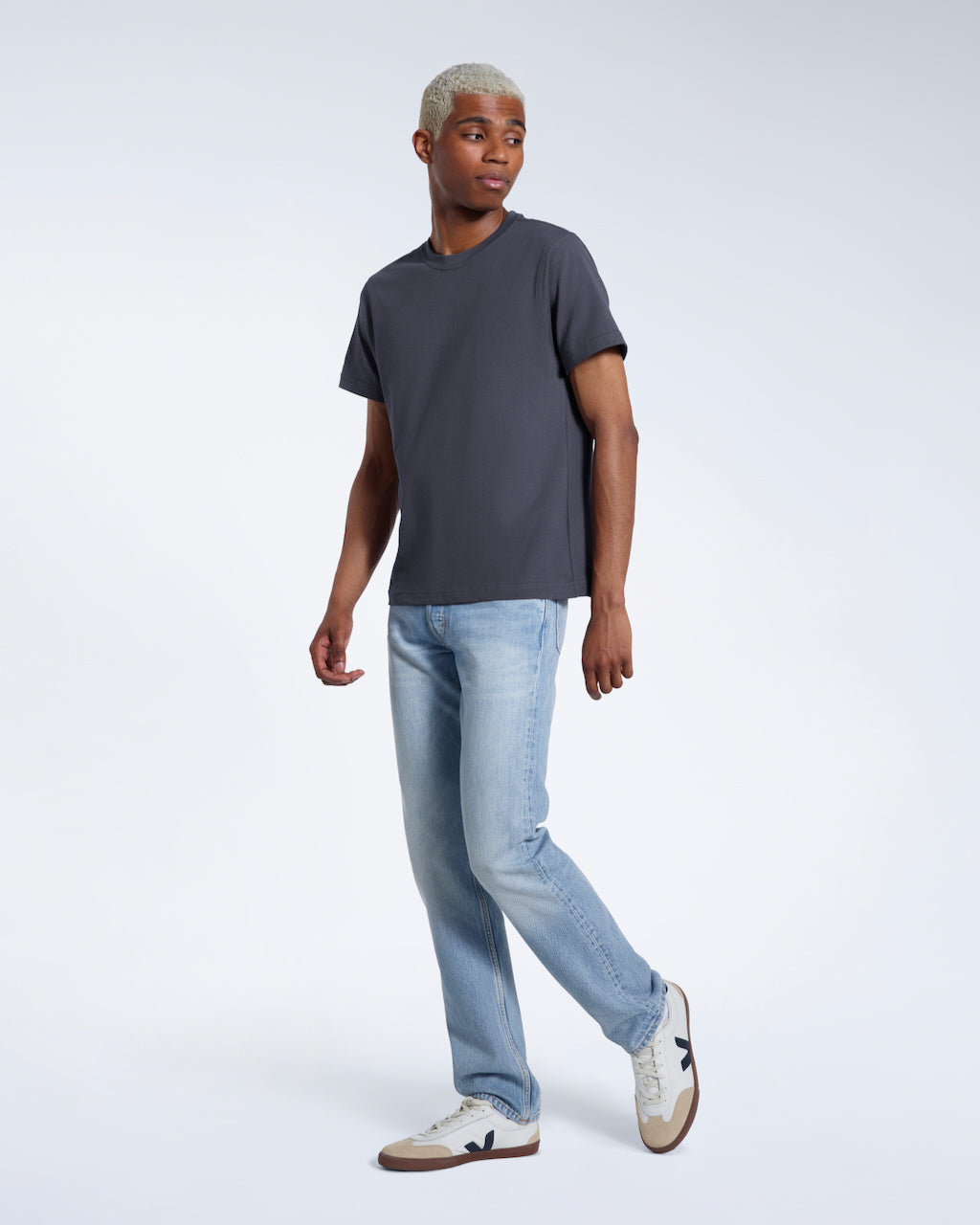 A full body photo of a man looking to the side, modelling a plain dark grey short sleeve organic cotton t shirt.