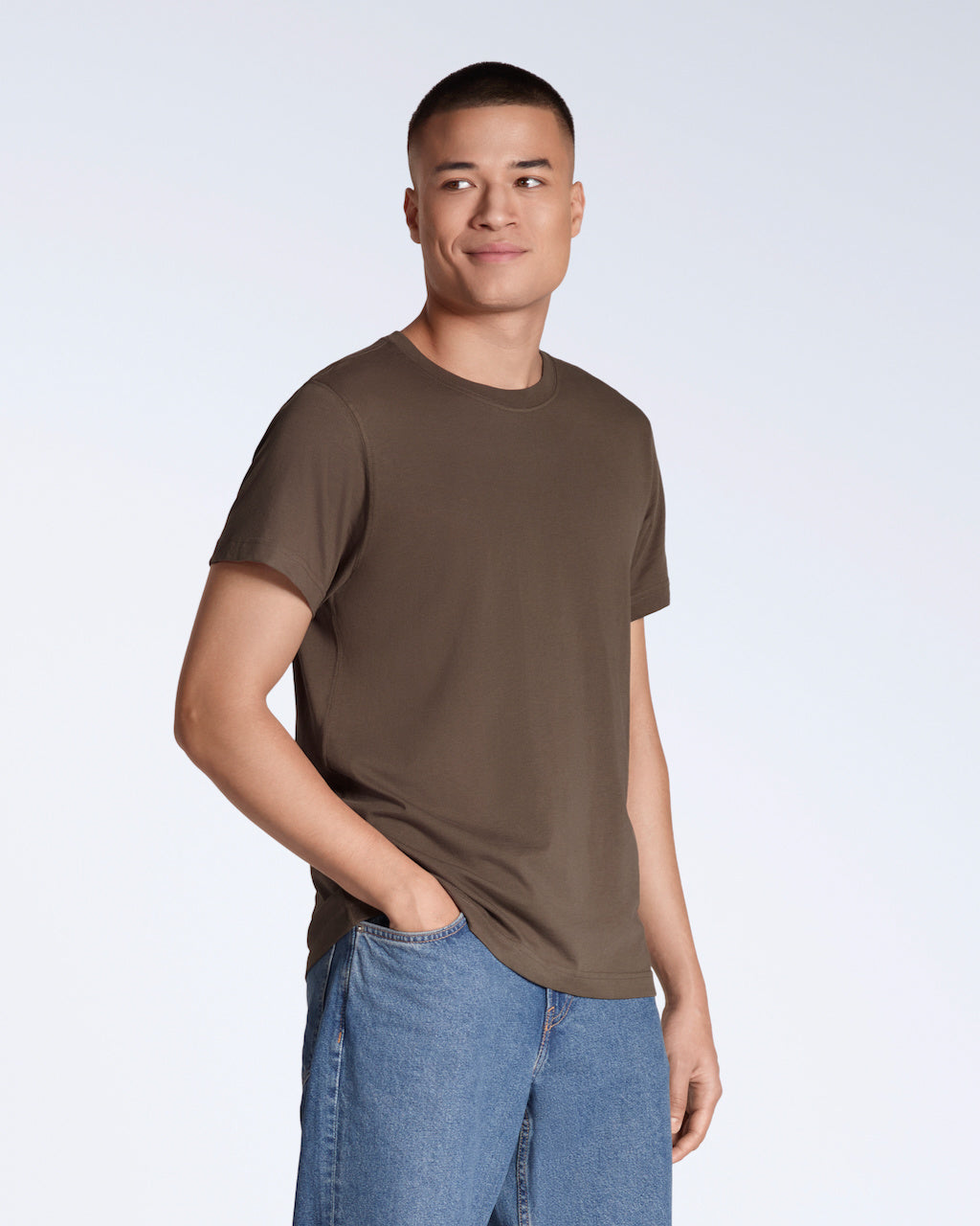 A man smiling with his hand in his pocket, modelling a plain brown, short sleeve organic cotton t shirt.