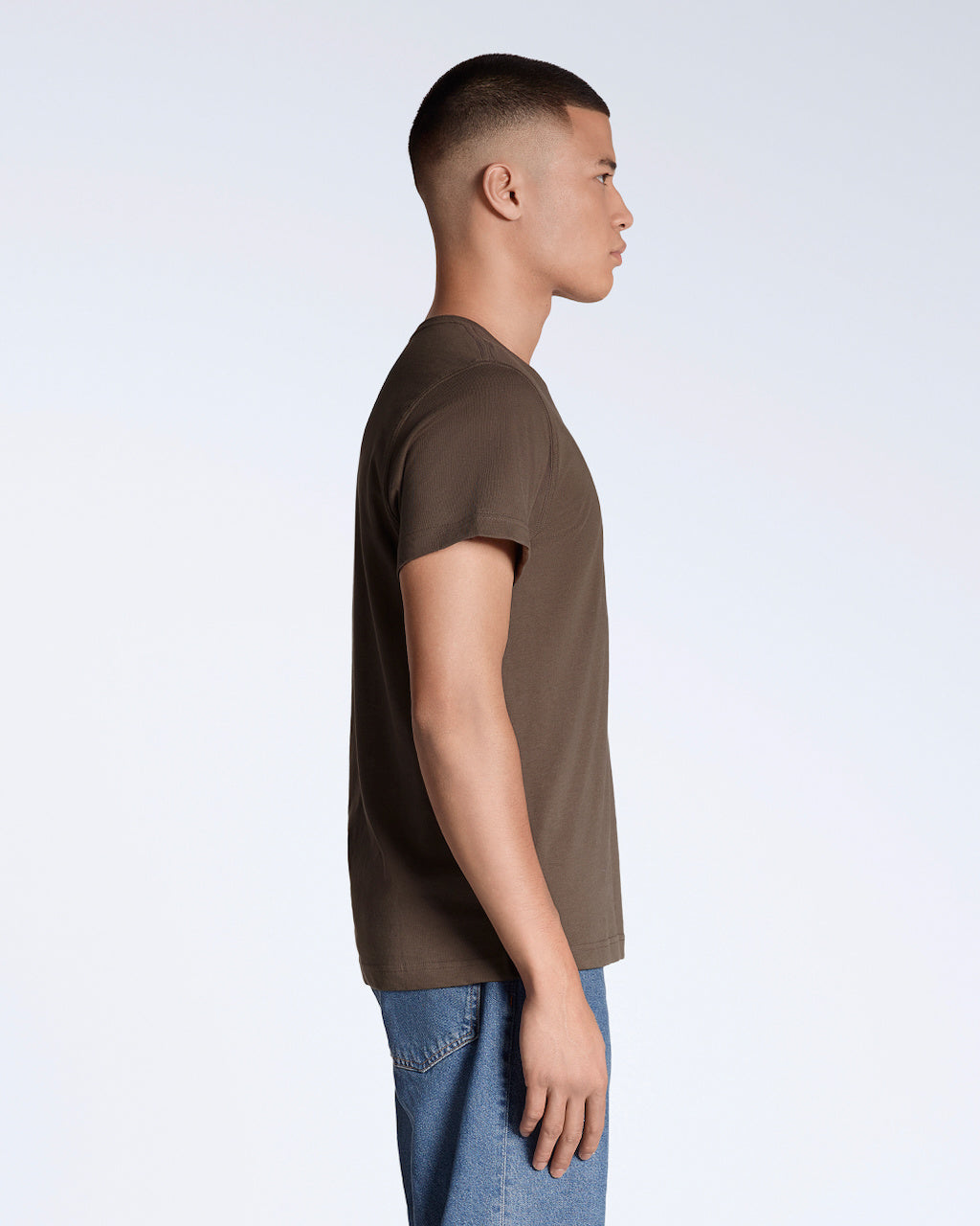 A man facing side on, modelling a plain brown short sleeve organic cotton t shirt.