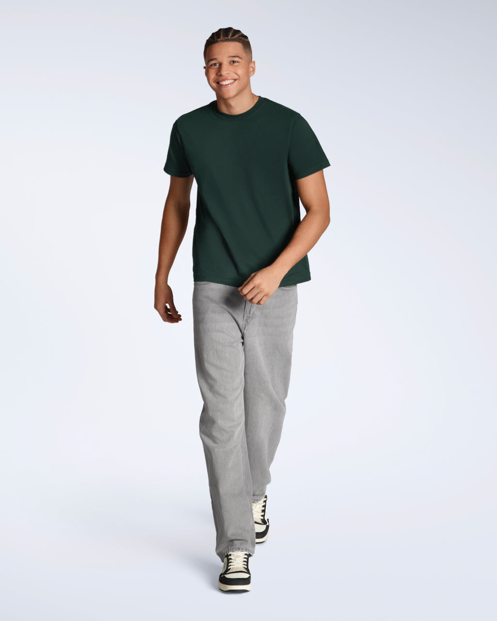 A full body photo of a man smiling and walking towards the camera, modelling a plain green, short sleeve organic cotton t shirt with a pair of jeans.