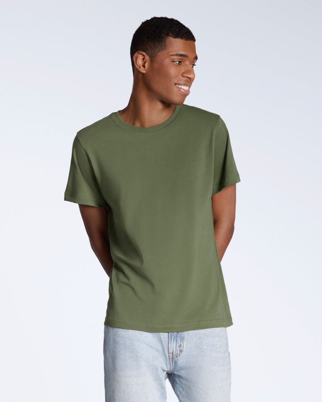 A man smiling with his arms behind his back, modelling a plain khaki green short sleeve organic cotton t shirt.