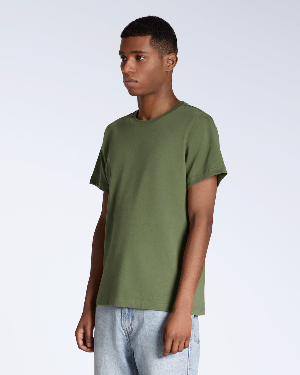A man at an angle with his arms by his sides, modelling a plain khaki green short sleeve organic cotton t shirt.