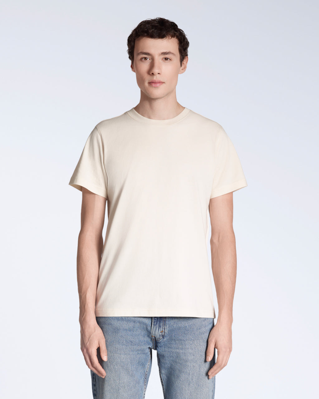 A man facing front on looking into the camera, modelling a plain, natural coloured, organic cotton t shirt.