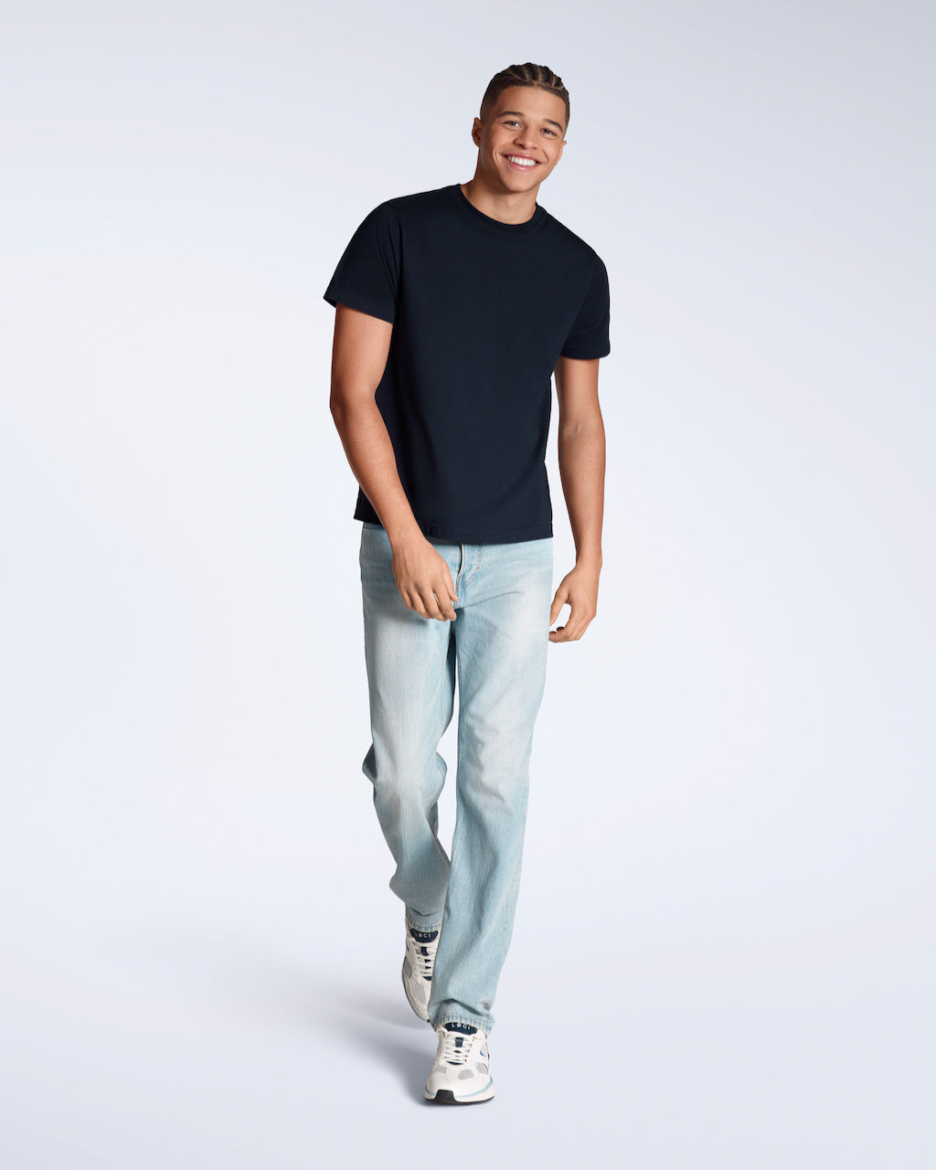 A full body photo of a man smiling, walking towards the camera, modelling a plain navy, short sleeve organic cotton t shirt with a pair of jeans.