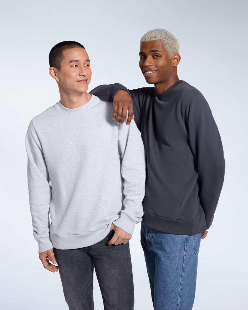 Two men smiling, modelling plain grey and dark grey, organic cotton sweatshirts.