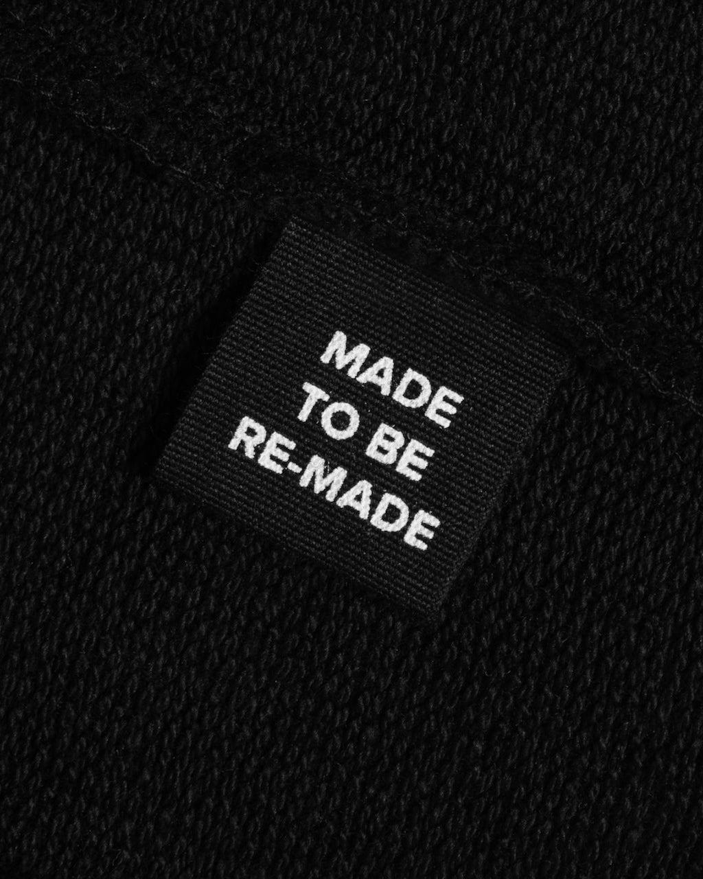 A close up of a label tag in a black organic cotton sweatshirt that says 'made to be re made'.