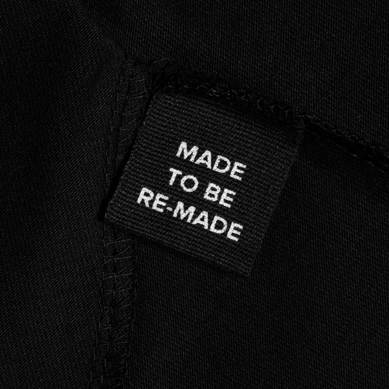A close up of a label tag in a black organic cotton t shirt dress that says 'made to be re made'.