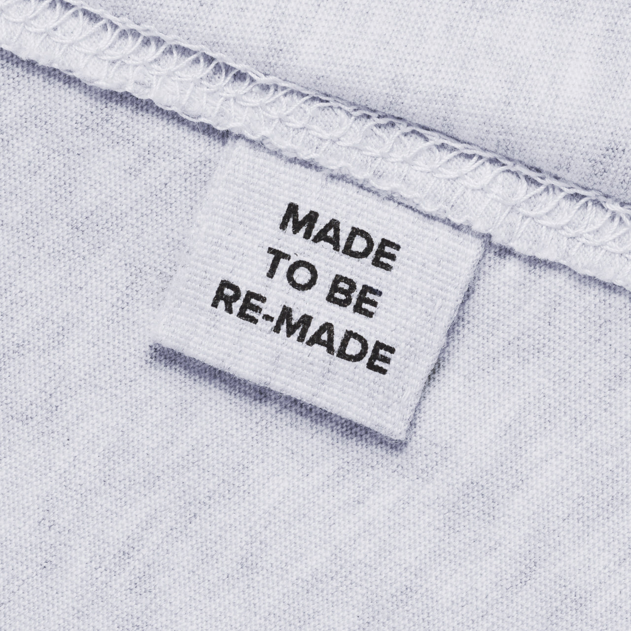 A close up of a label tag in a grey organic cotton t shirt that says 'made to be re made'.