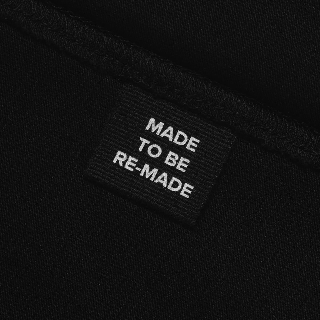 A close up of a label tag in a black organic cotton hoodie that says 'made to be re made'.