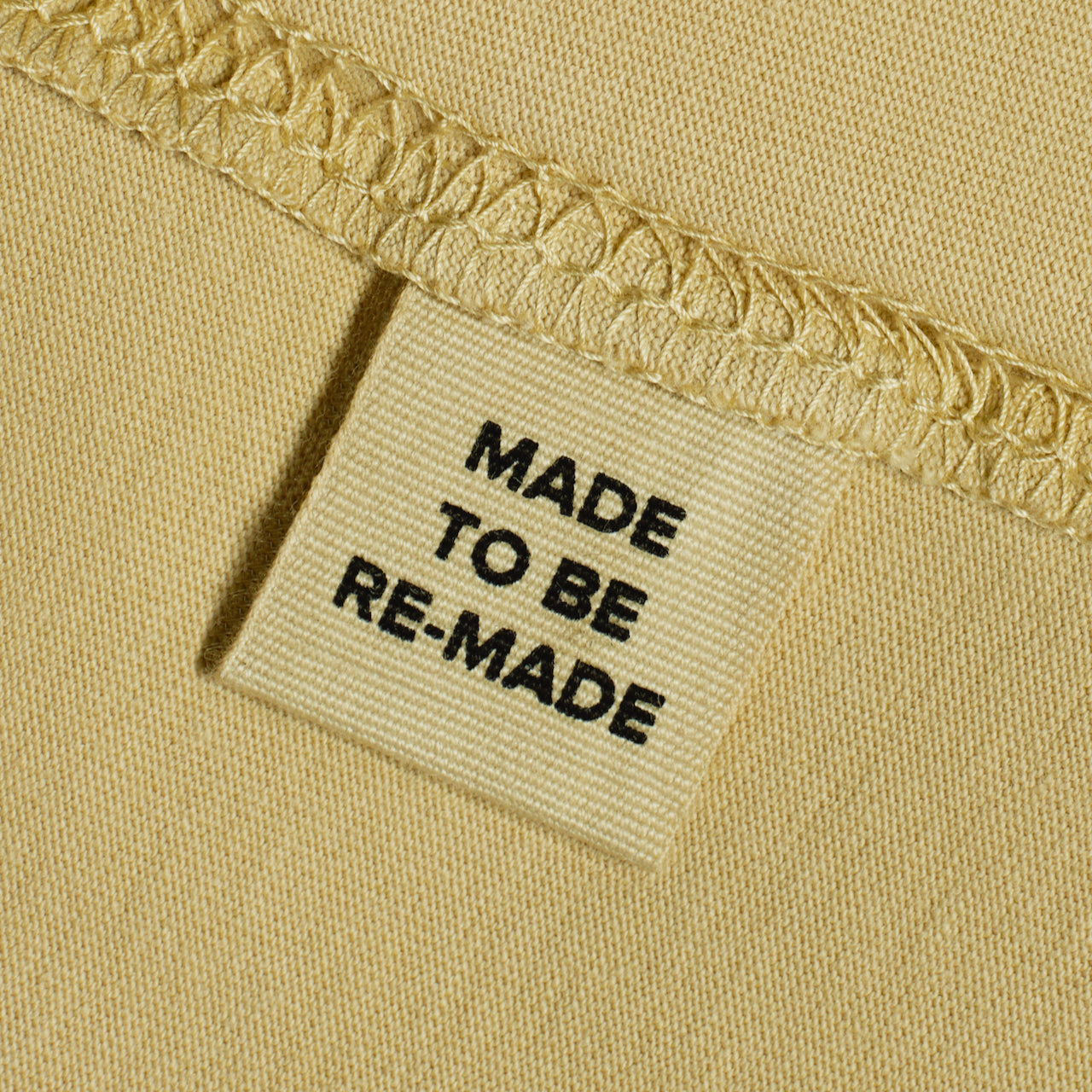 A close up of a label tag in a light khaki organic cotton t shirt that says 'made to be re made'.
