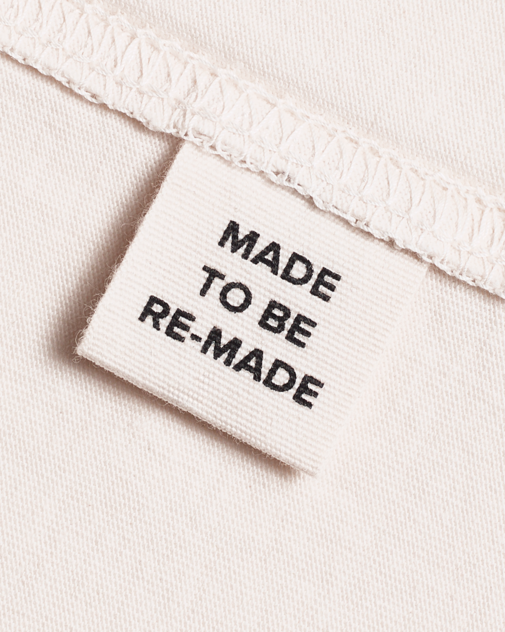 A close up of a label tag in a natural coloured, organic cotton t shirt that says 'made to be re made'.