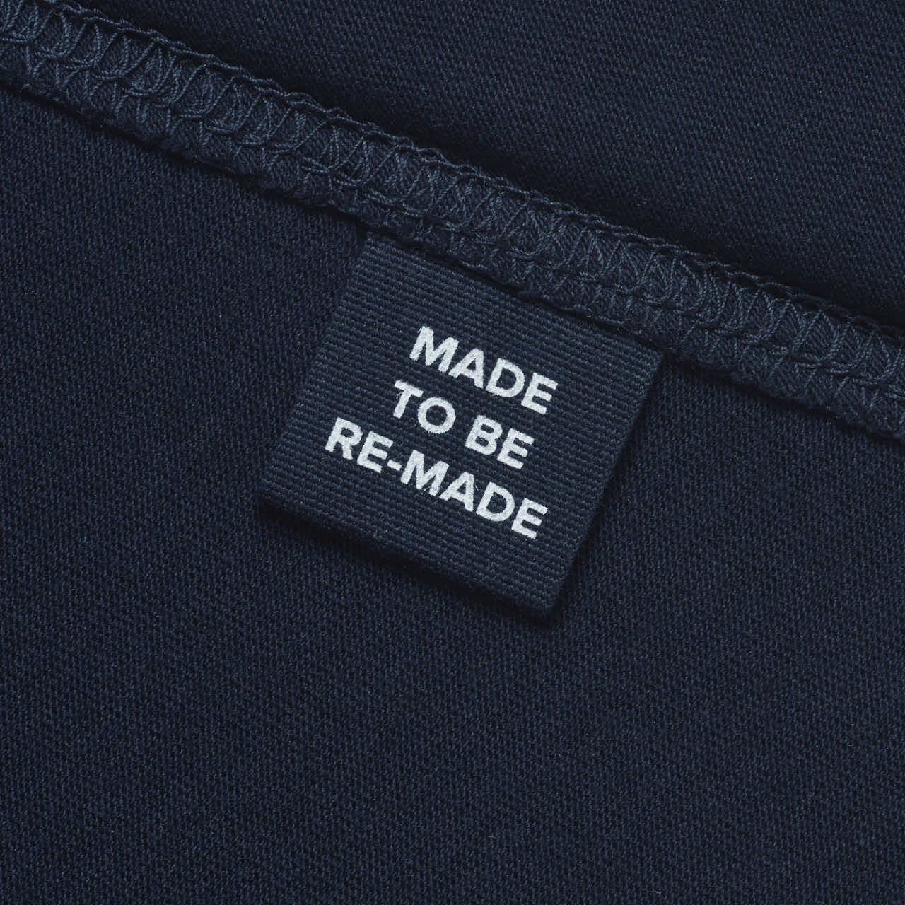 A close up of a label tag in a navy organic cotton t shirt that says 'made to be re made'.