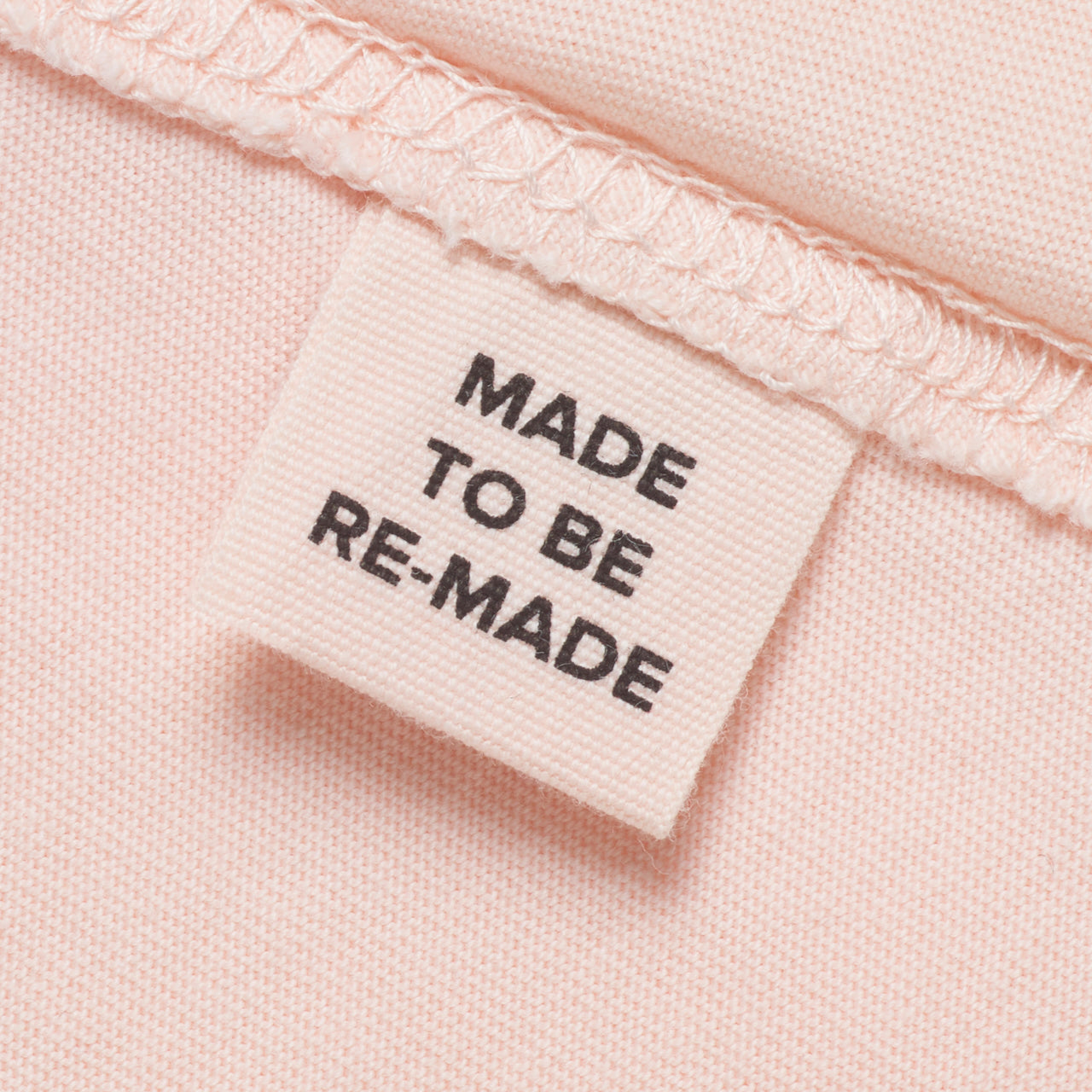 A close up of a label tag in a pink organic cotton t shirt that says 'made to be re made'.