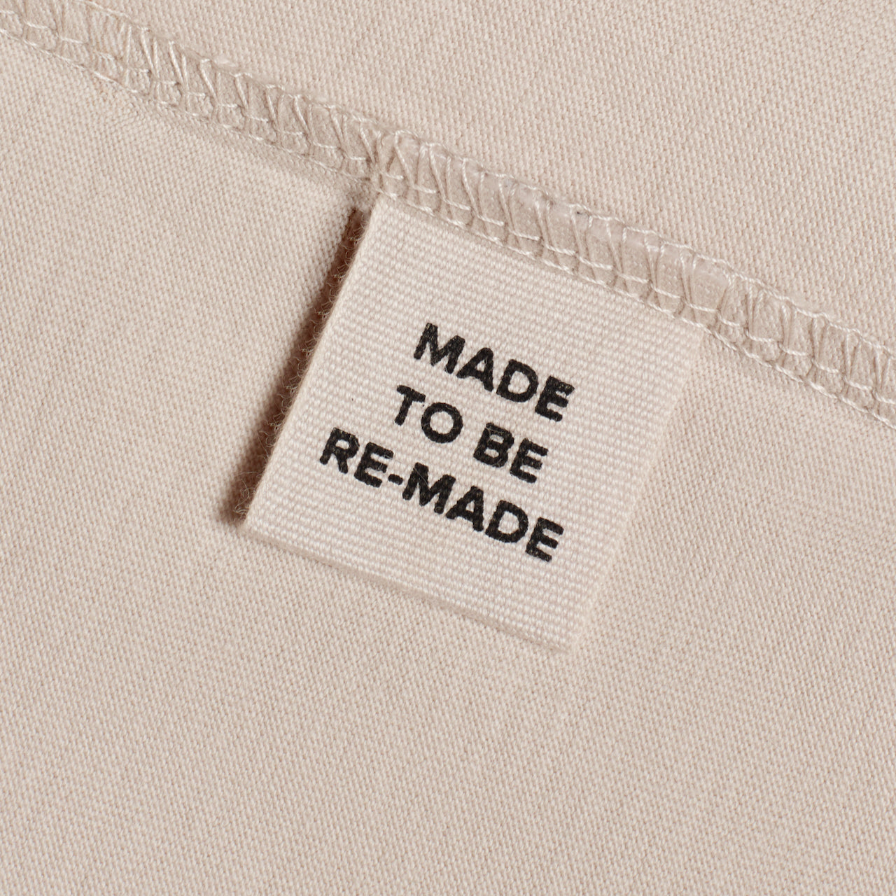 A close up of a label tag in an ecru organic cotton t shirt that says 'made to be re made'.
