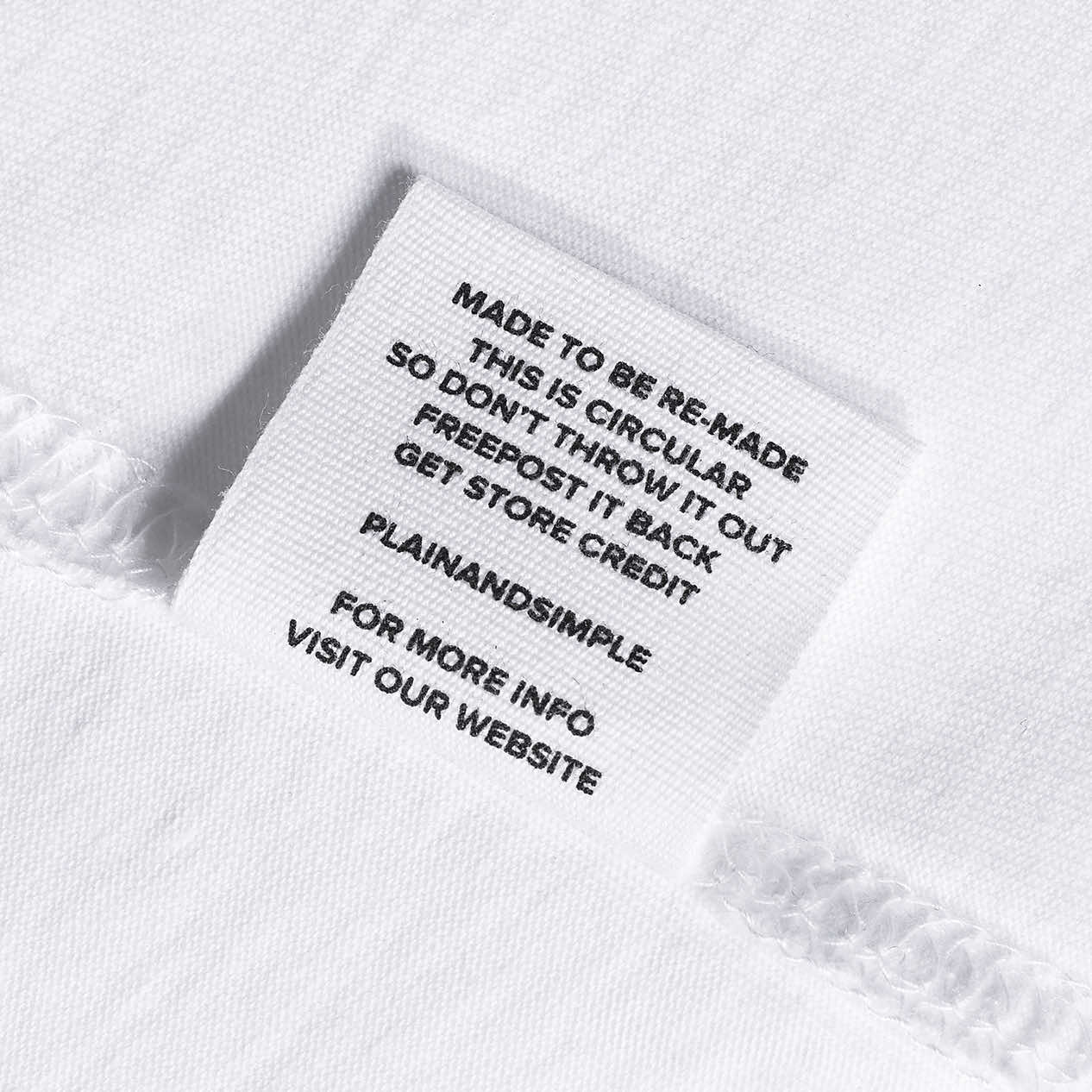 A close-up of a label in a white organic cotton t shirt, saying 'made to be re made this is circular so don't throw it out freepost it back get store credit'