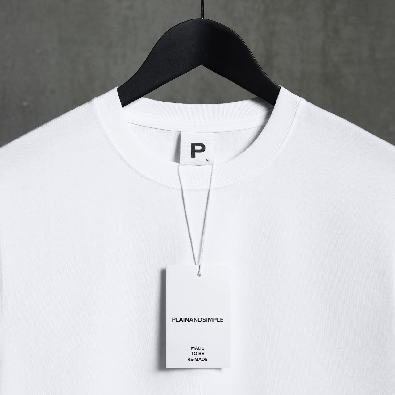 A close up of the label tag and neckline of a plain white organic cotton t shirt on a hanger.