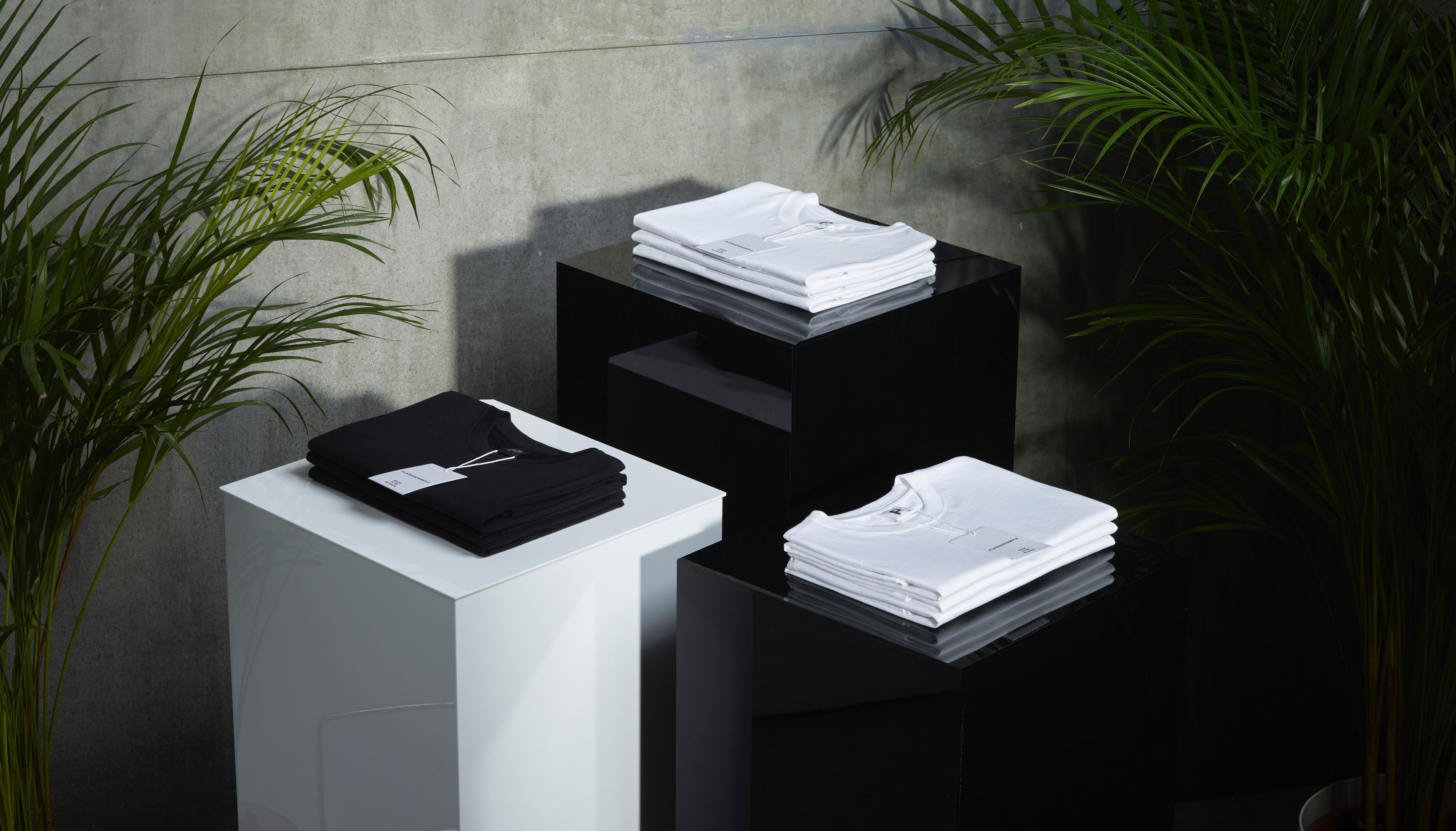 3 plinths, with folded plain black and white organic cotton t shirts on top.