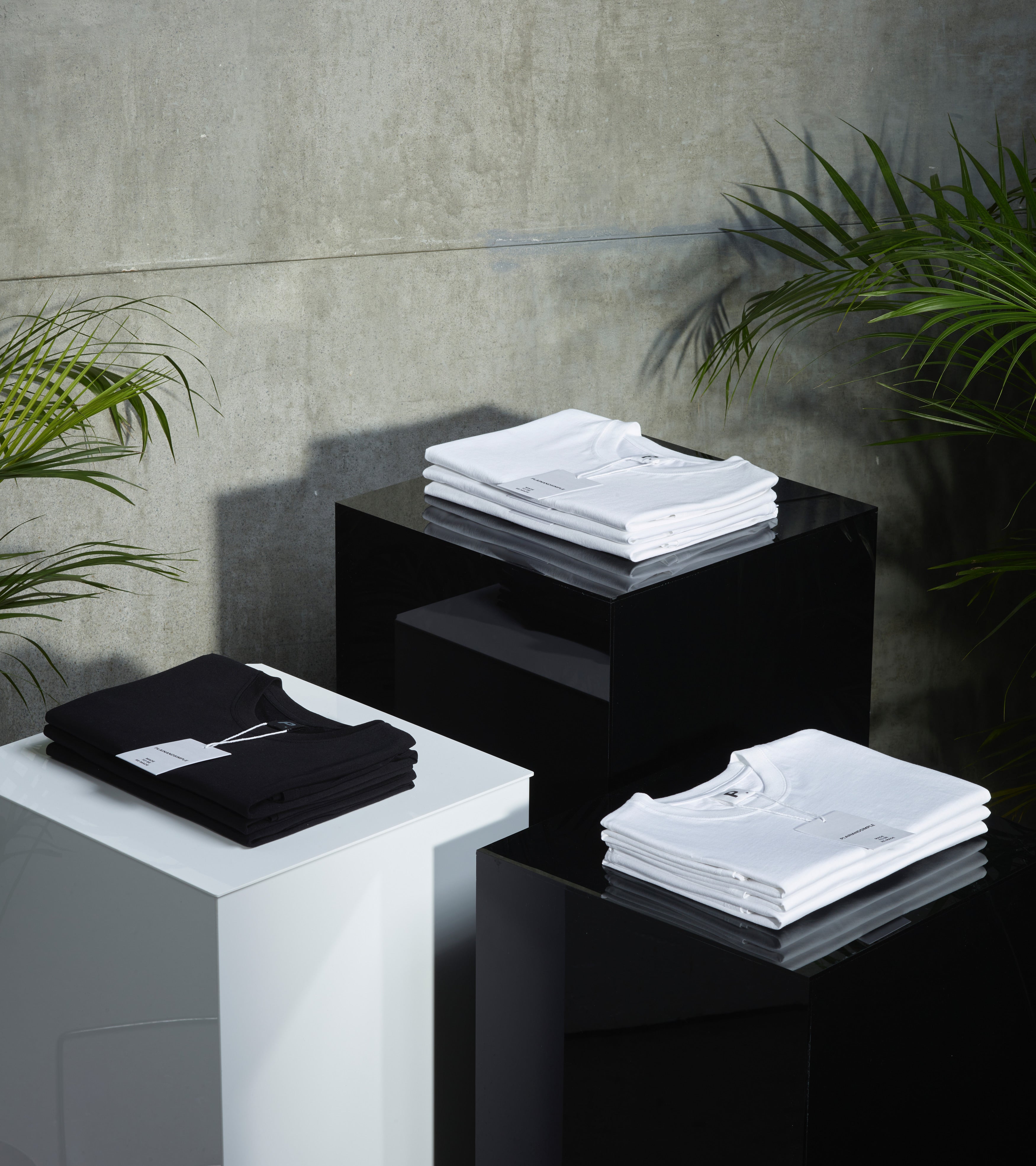 3 plinths, with folded plain black and white organic cotton t shirts on top.