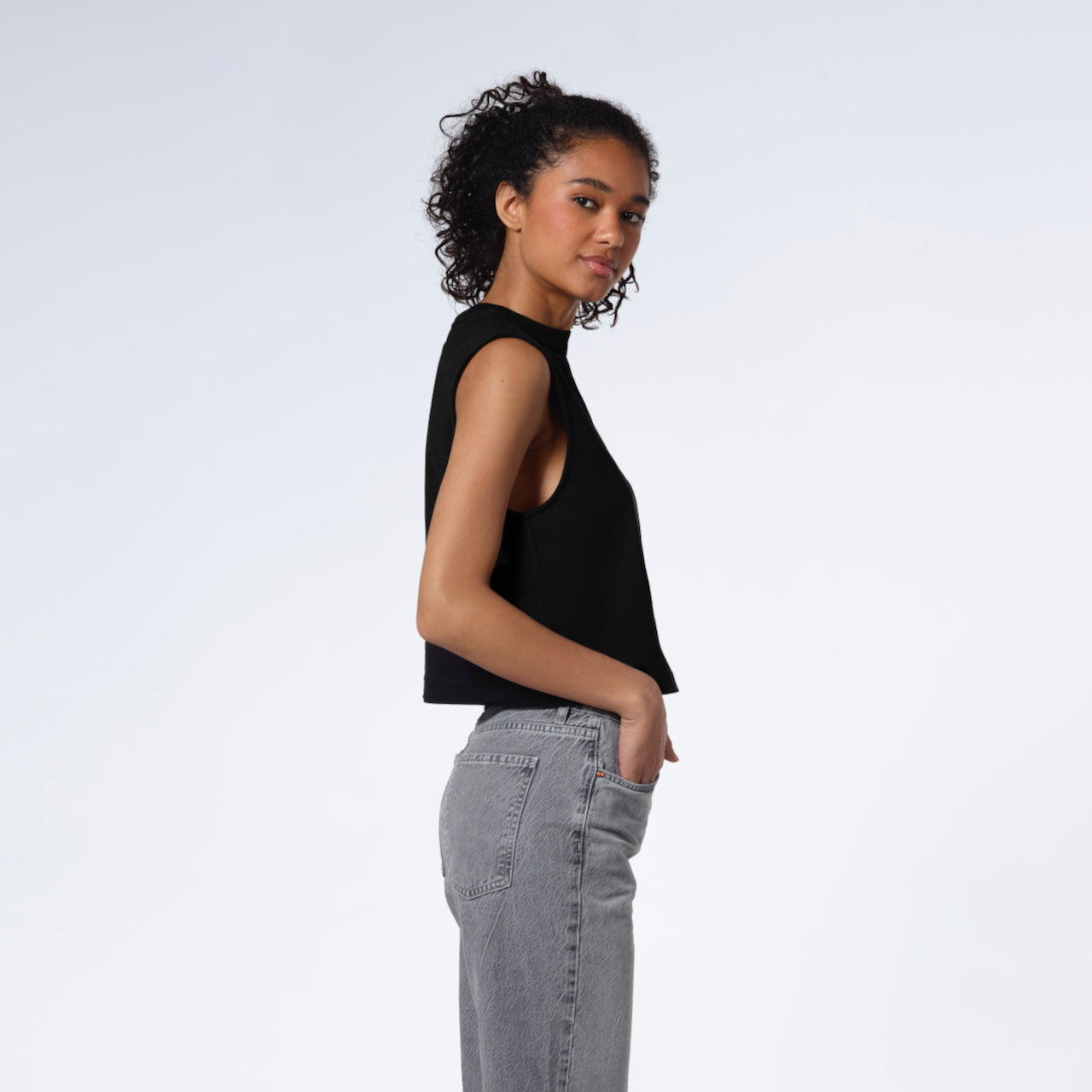 A woman facing side on and looking at the camera, modelling a plain black sleeveless organic cotton tank top.