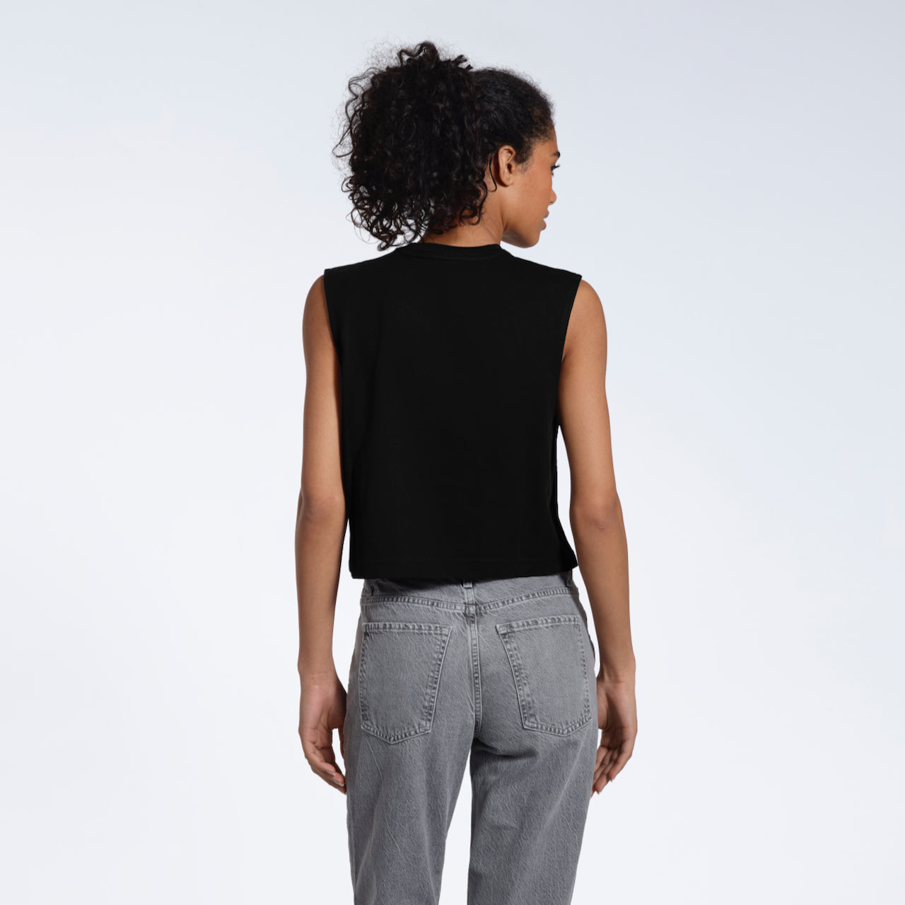 A woman with her back to the camera, modelling a plain black sleeveless organic cotton tank top.