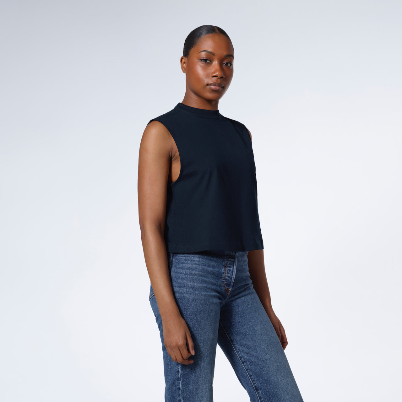 A woman looking into the camera with her hands by her sides, modelling a plain navy sleeveless organic cotton tank top.