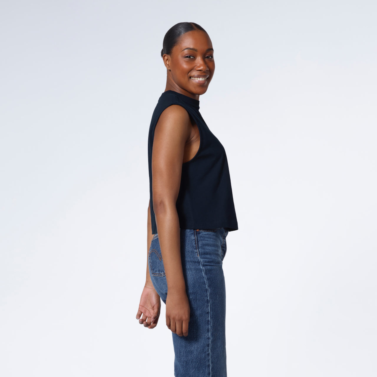 A woman facing side on and looking at the camera, modelling a plain navy sleeveless organic cotton tank top.