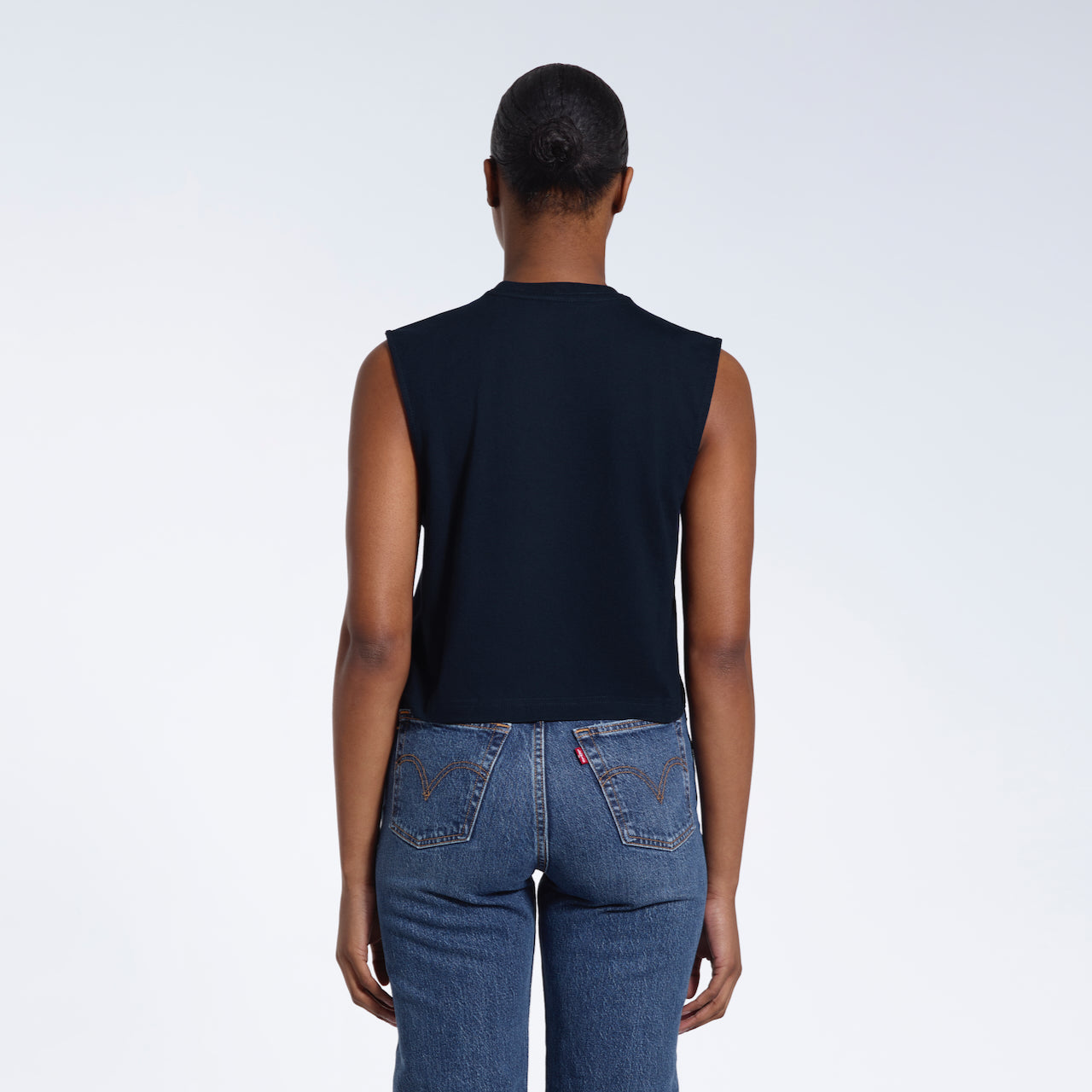 A woman with her back to the camera, modelling a plain navy sleeveless organic cotton tank top.