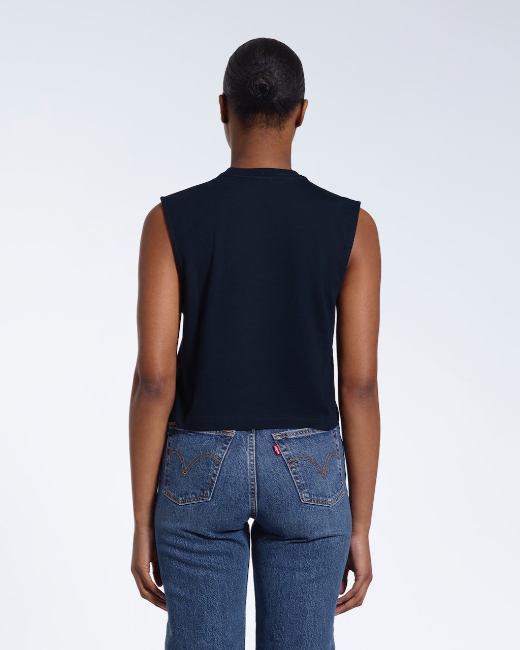A woman with her back to the camera, modelling a plain navy sleeveless organic cotton tank top.