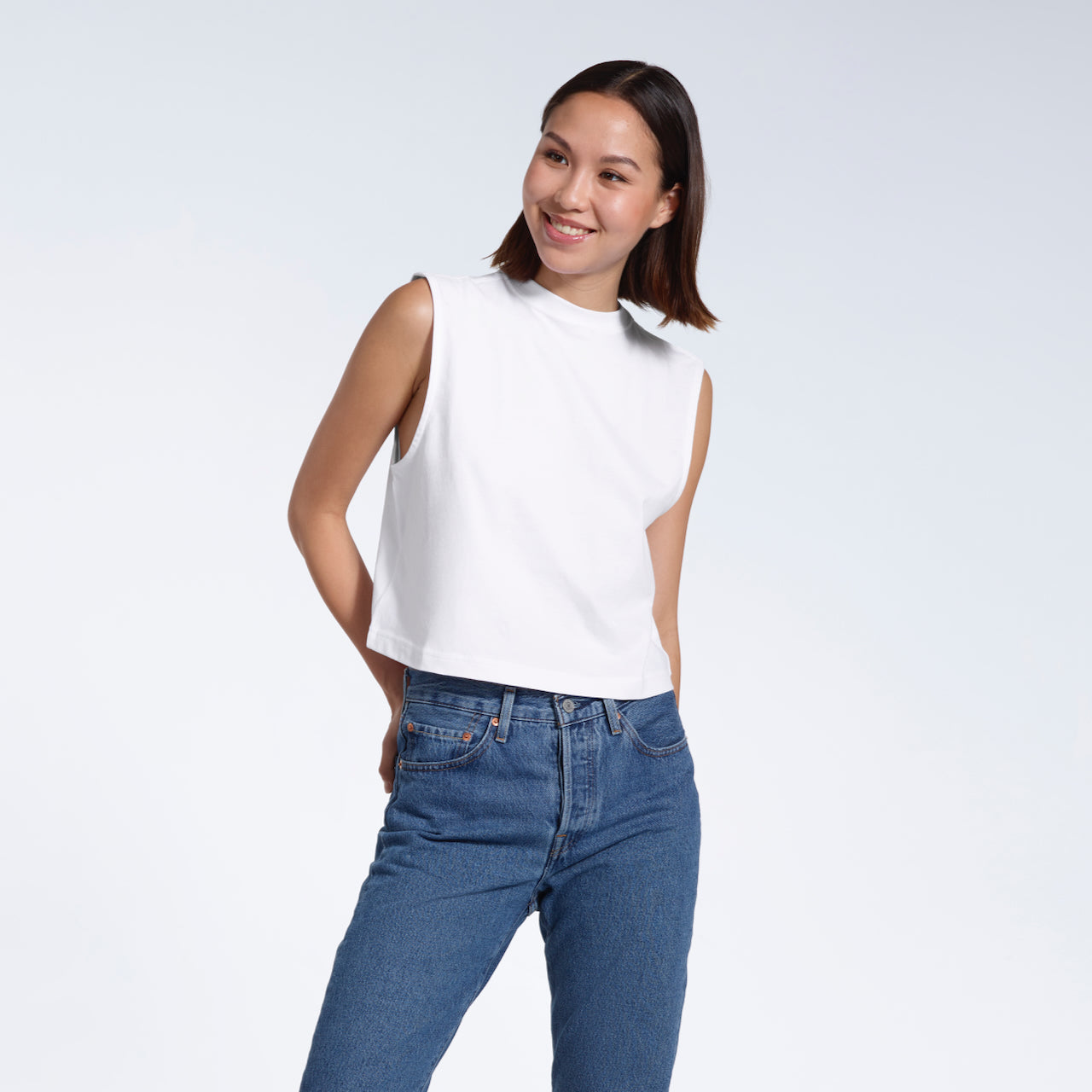 A woman smiling, modelling a plain white sleeveless organic cotton tank top.