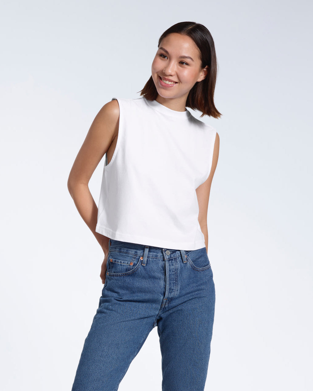 A woman smiling, modelling a plain white sleeveless organic cotton tank top.
