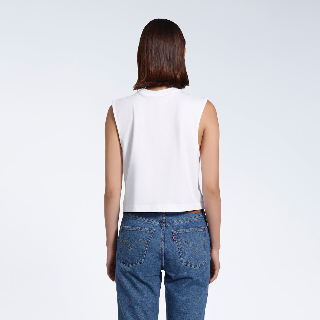 A woman with her back to the camera, modelling a plain white sleeveless organic cotton tank top.