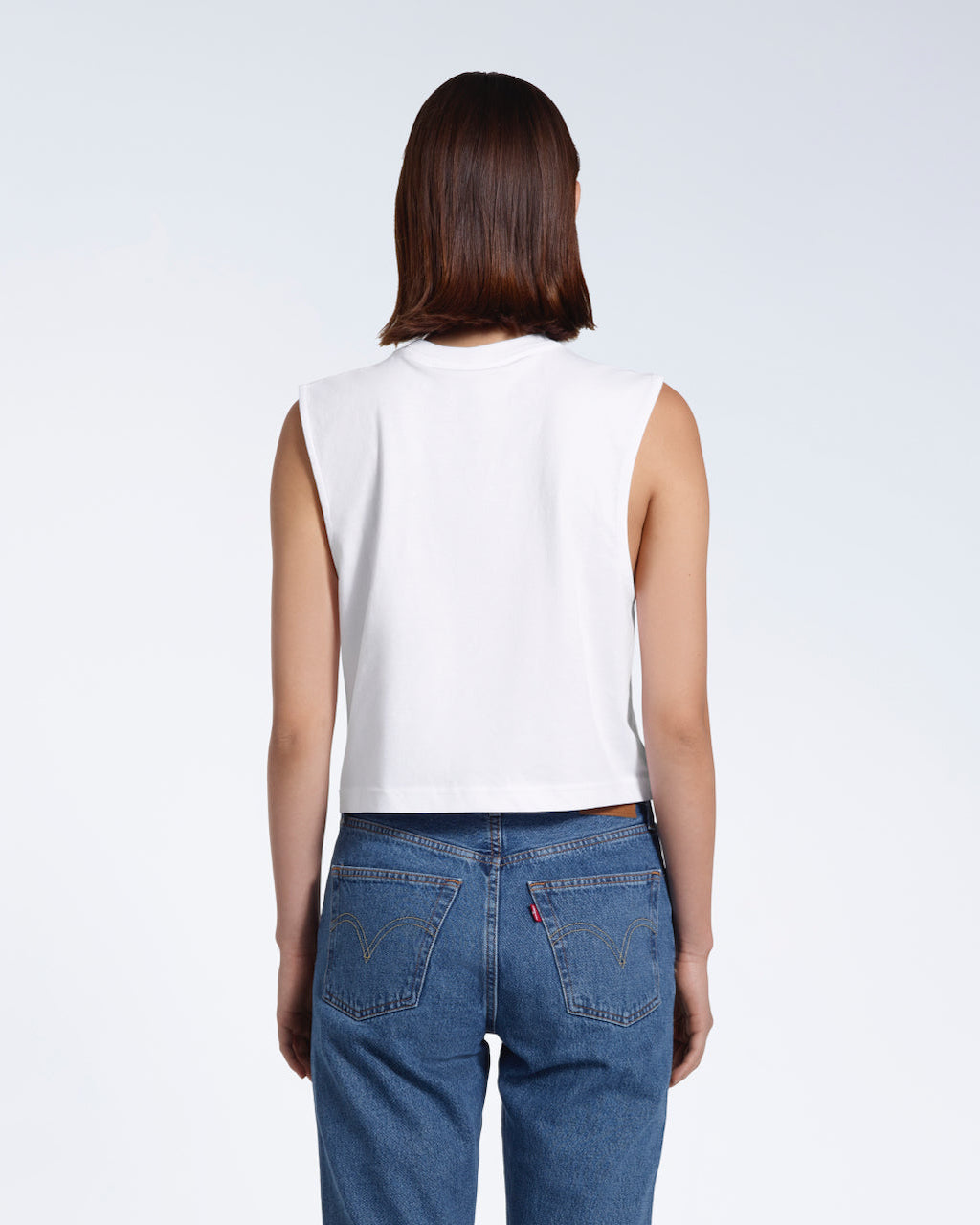 A woman with her back to the camera, modelling a plain white sleeveless organic cotton tank top.