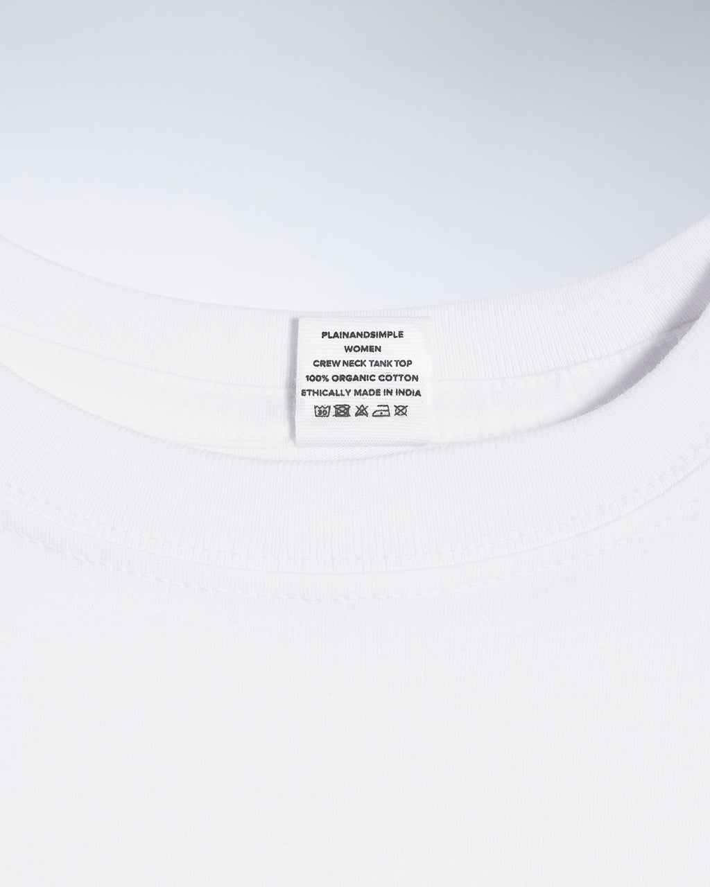 A close up of a neck label in a women's white sleeveless organic cotton crew neck tank top.