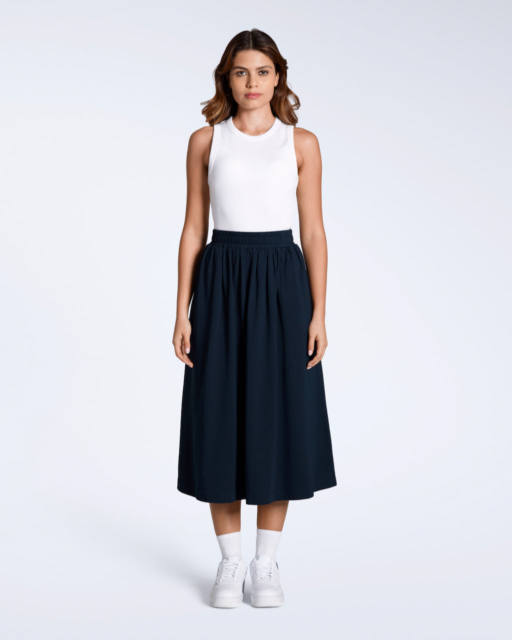 A full body photo of a woman looking into the camera with her arms by her side, modelling a flowy, navy, organic cotton midi skirt.