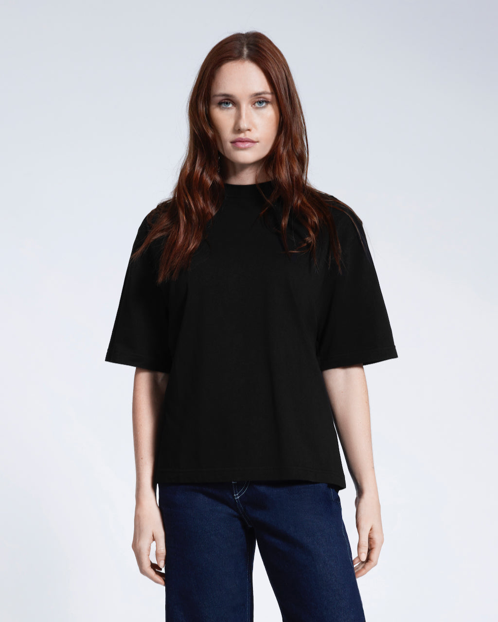 A woman face on looking into the camera, modelling a plain black boxy heavyweight organic cotton t shirt.