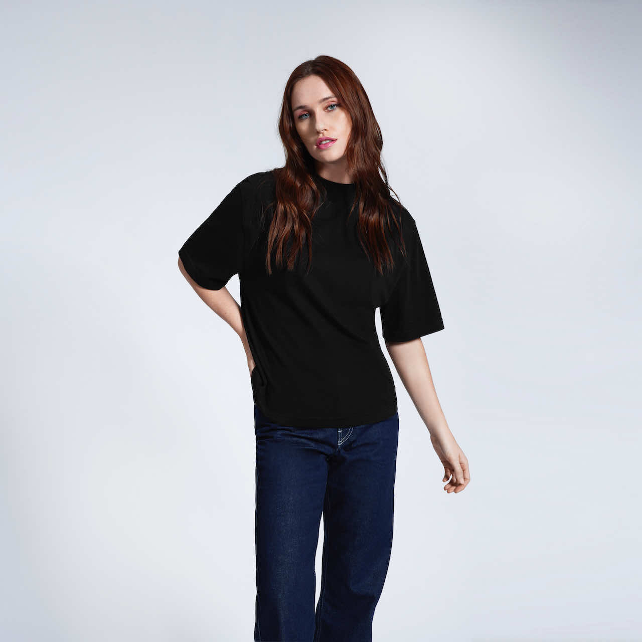 A woman with her hand by her hip looking into the camera, modelling a plain black boxy heavyweight organic cotton t shirt.