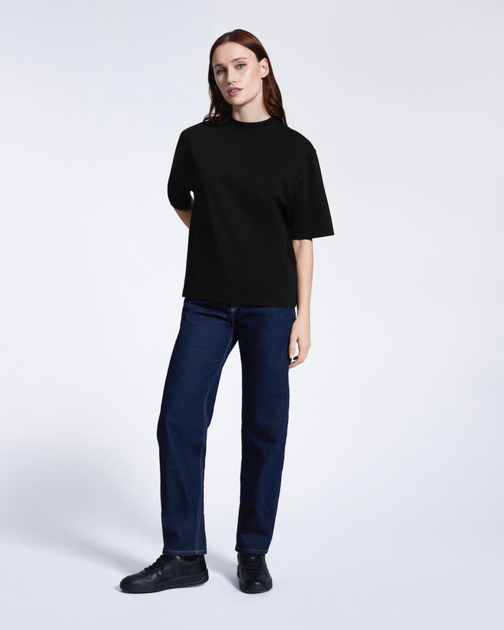A full body photo of a woman looking into the camera, modelling a plain black boxy heavyweight organic cotton t shirt.
