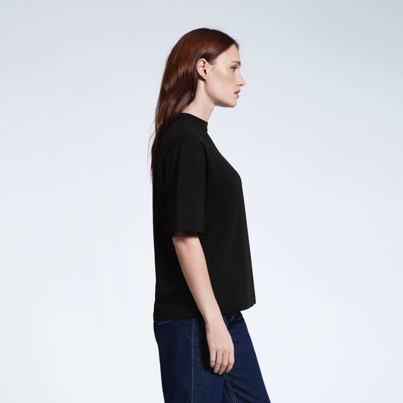 A woman side on, modelling a plain black boxy heavyweight organic cotton t shirt.