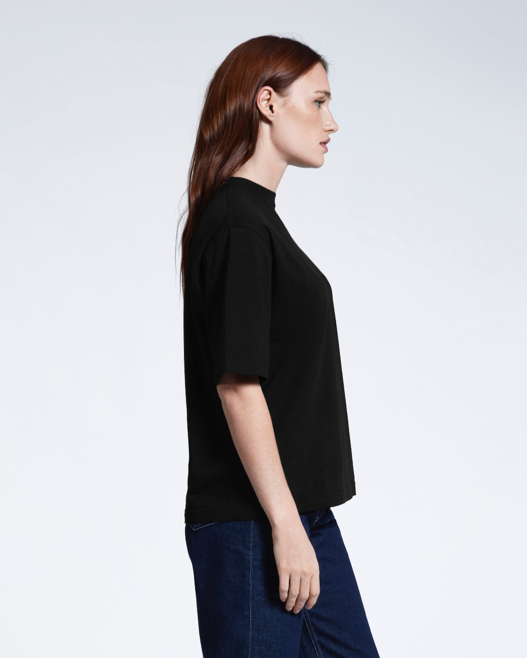 A woman side on, modelling a plain black boxy heavyweight organic cotton t shirt.