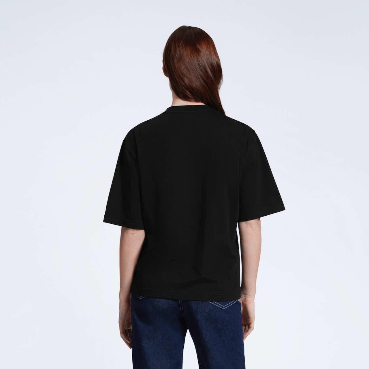 A woman facing away from the camera, modelling a plain black boxy heavyweight organic cotton t shirt.