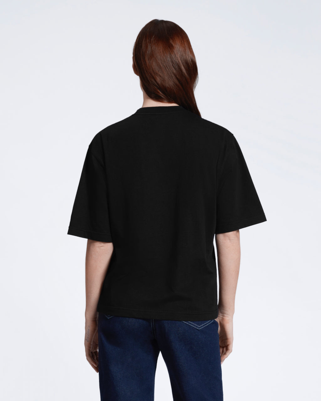 A woman facing away from the camera, modelling a plain black boxy heavyweight organic cotton t shirt.
