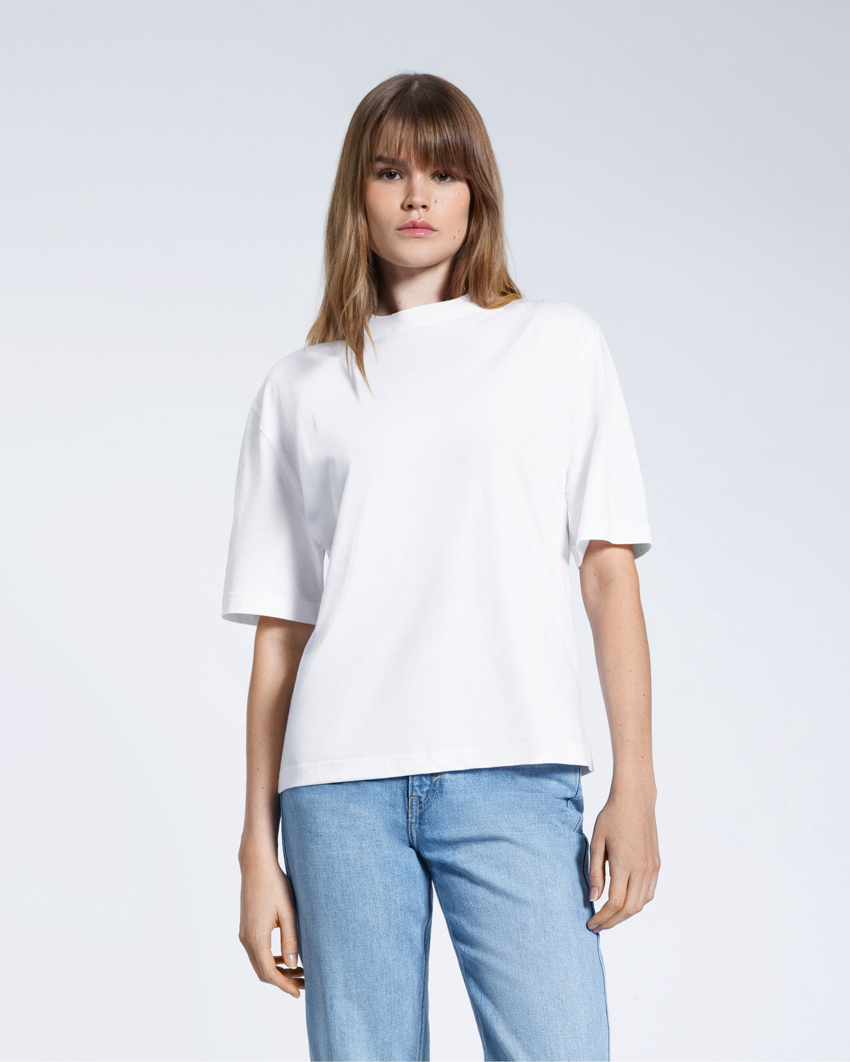 A woman face on looking into the camera, modelling a plain white boxy heavyweight organic cotton t shirt.