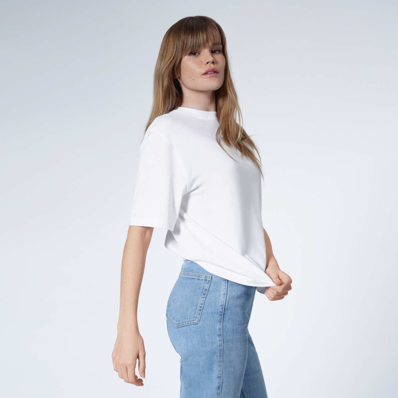 A woman looking into the camera, touching her plain white boxy heavyweight organic cotton t shirt.