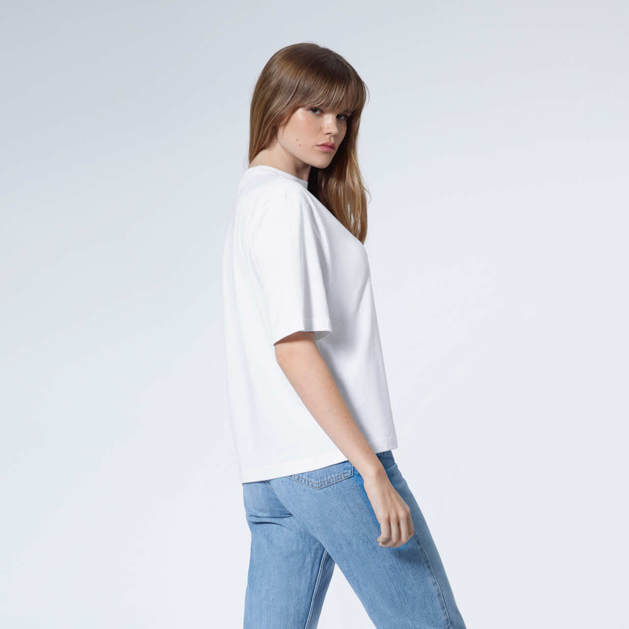 A woman turned to face the camera, modelling a plain white boxy heavyweight organic cotton t shirt.
