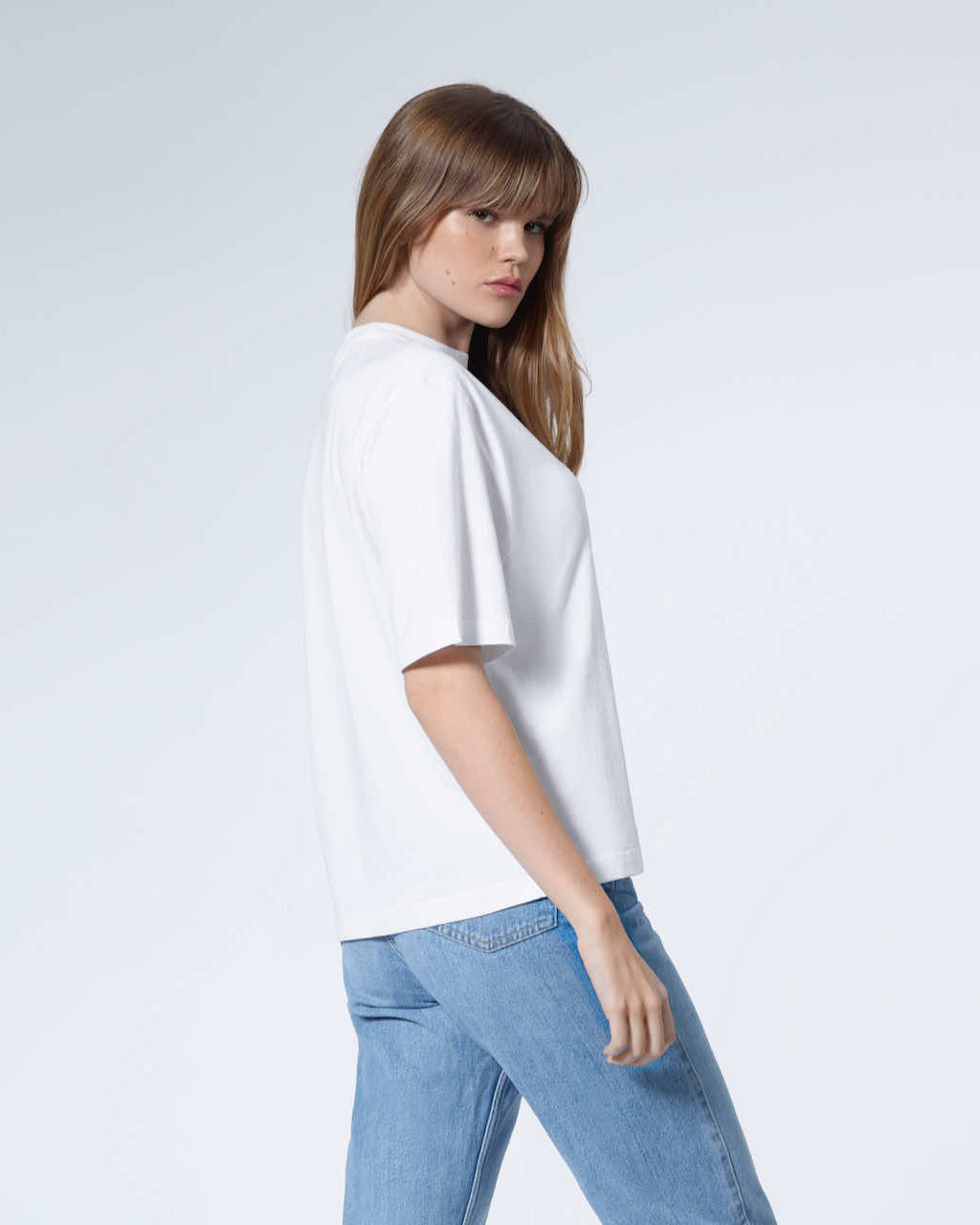 A woman turned to face the camera, modelling a plain white boxy heavyweight organic cotton t shirt.