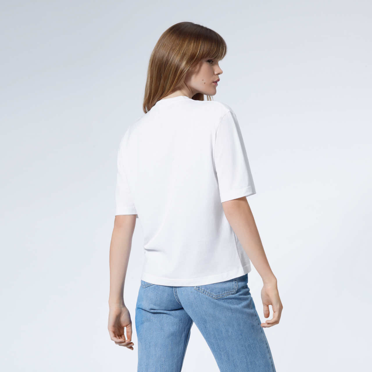 A woman facing away from the camera, modelling a plain white boxy heavyweight organic cotton t shirt.