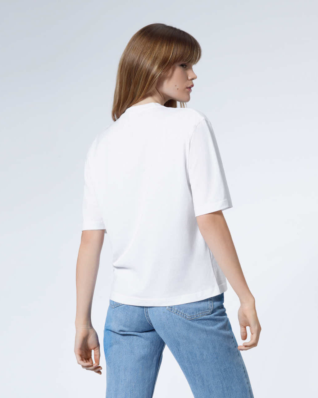 A woman facing away from the camera, modelling a plain white boxy heavyweight organic cotton t shirt.