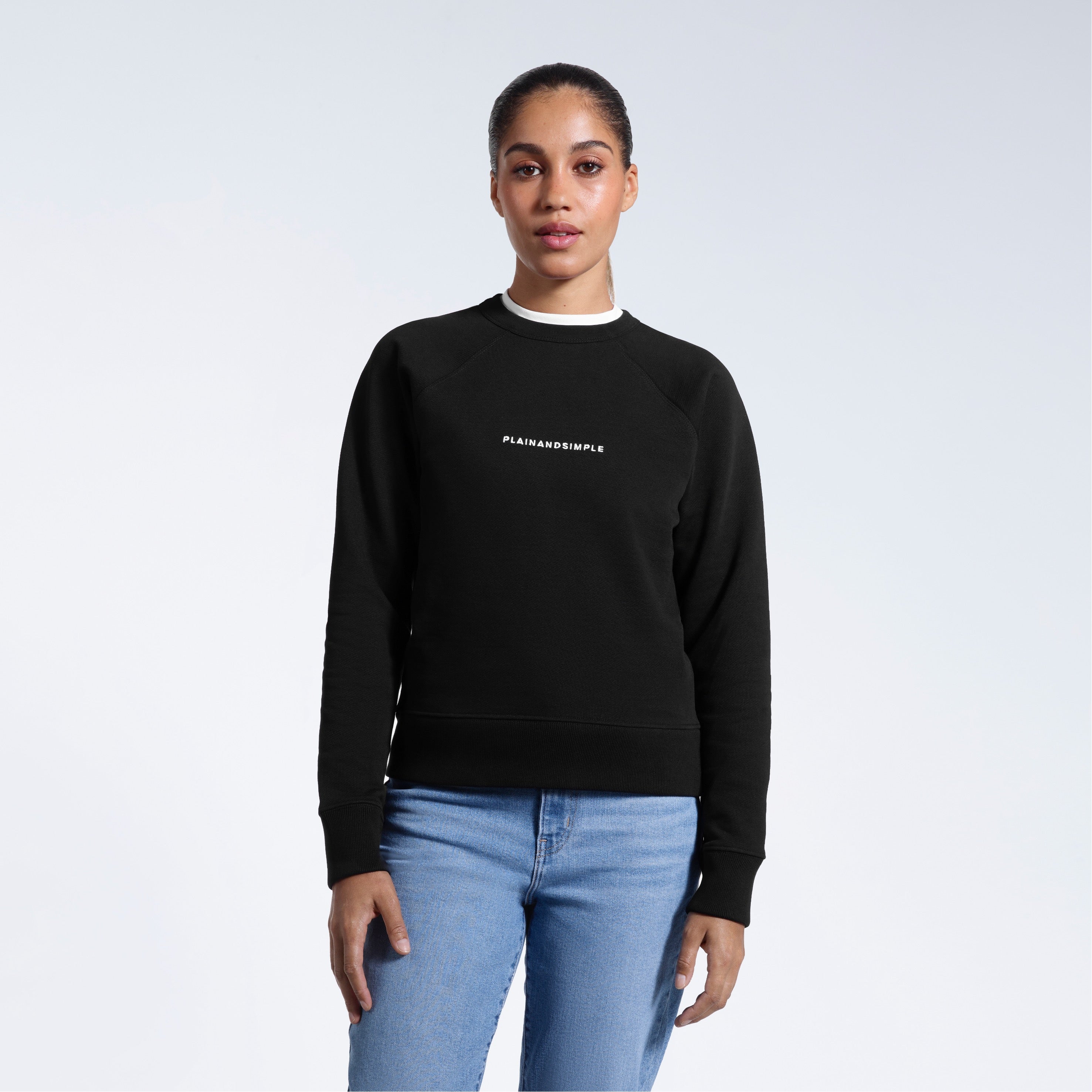 A woman face on with her arms by her side, modelling a branded black heavyweight organic cotton sweatshirt.